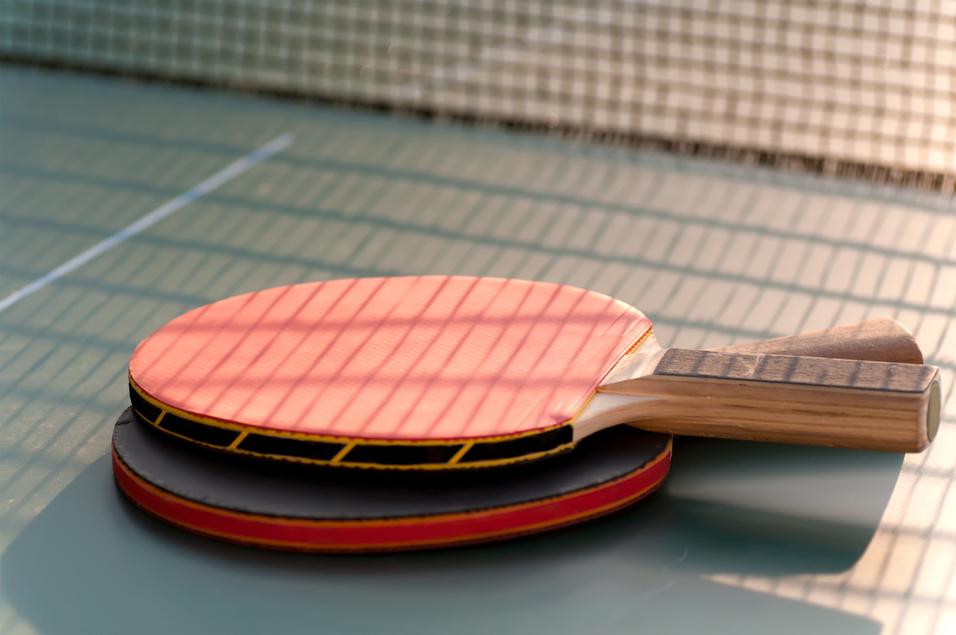 Nahaufnahme von zwei Tischtennisschlägern, einer mit roter und einer mit schwarzer Oberfläche, auf einer Tischtennisplatte.